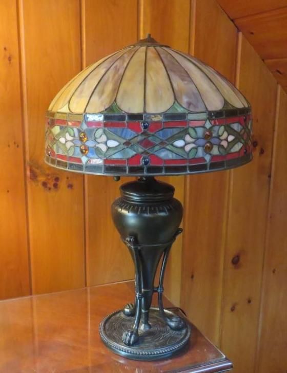 Tiffany-style stained glass lamp with ornate base on a wooden surface. The shade has a floral design.