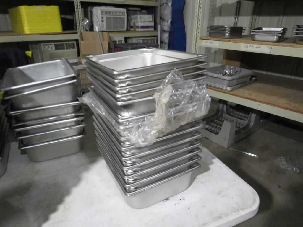 Stacks of stainless steel food pans on a white table in a storage area.
