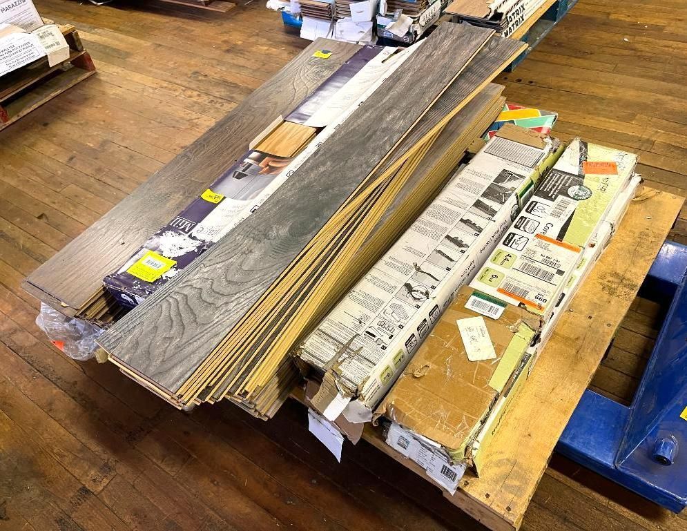 Pallet of gray and brown wood flooring planks and boxes on a wooden floor.