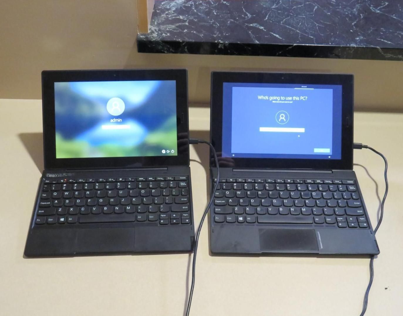 Two black laptops side by side, both displaying screens. One has a user login screen, the other a loading screen.