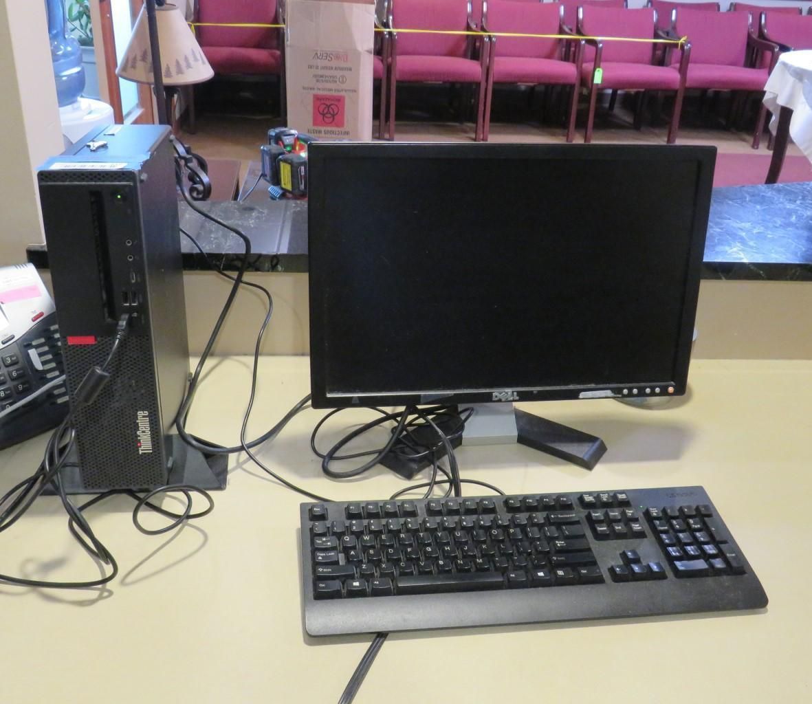 Computer setup on a desk: black tower, monitor, keyboard. In a room with chairs and a window.