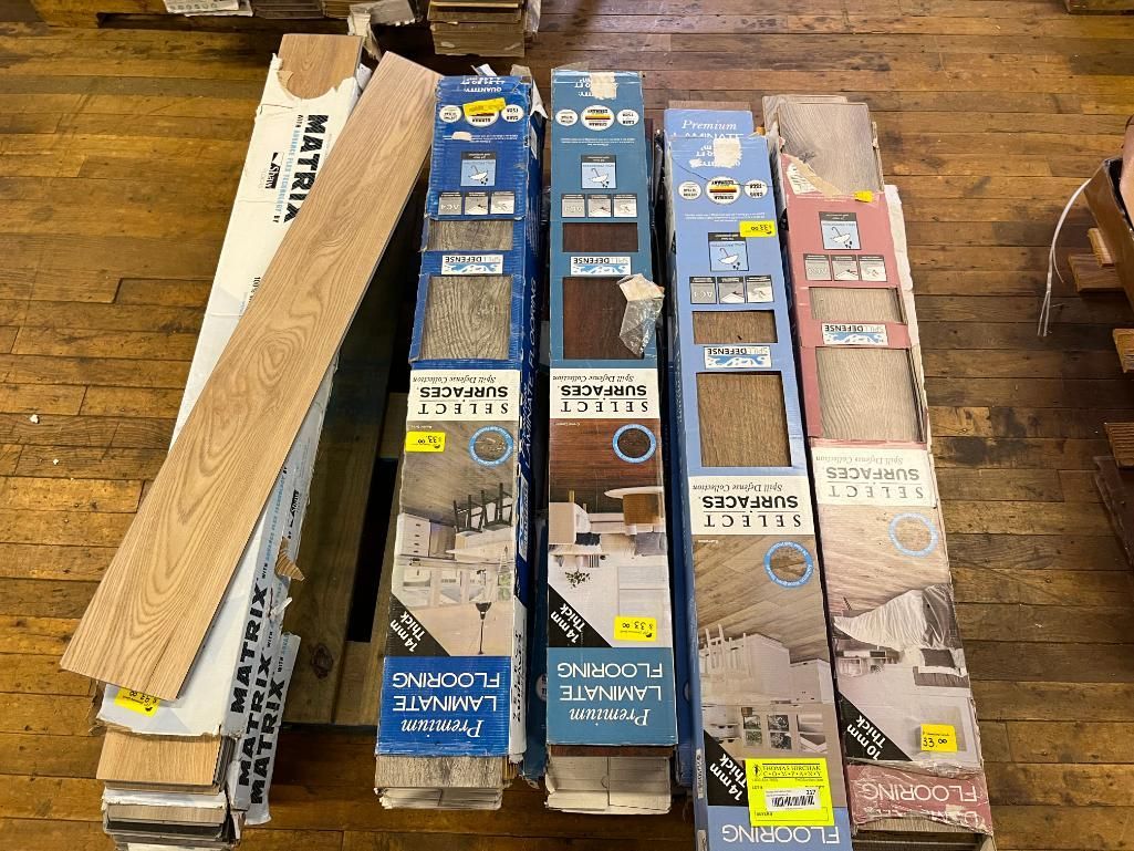 Several boxes of flooring samples on a wood floor. Some boxes are open, showing wood and stone patterns.