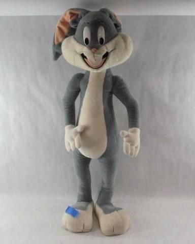 Plush Bugs Bunny standing, wearing a small bandage on his foot, with a slight smile.