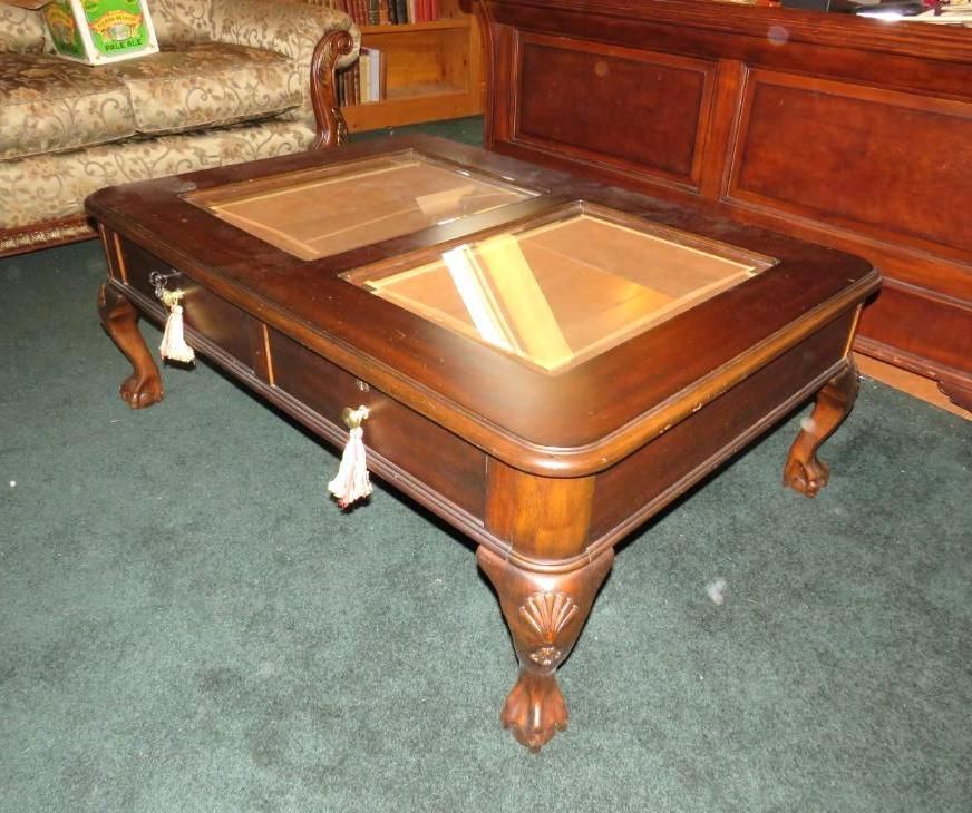 Wooden coffee table with glass top, drawers, and ornate carved legs, on green carpet.