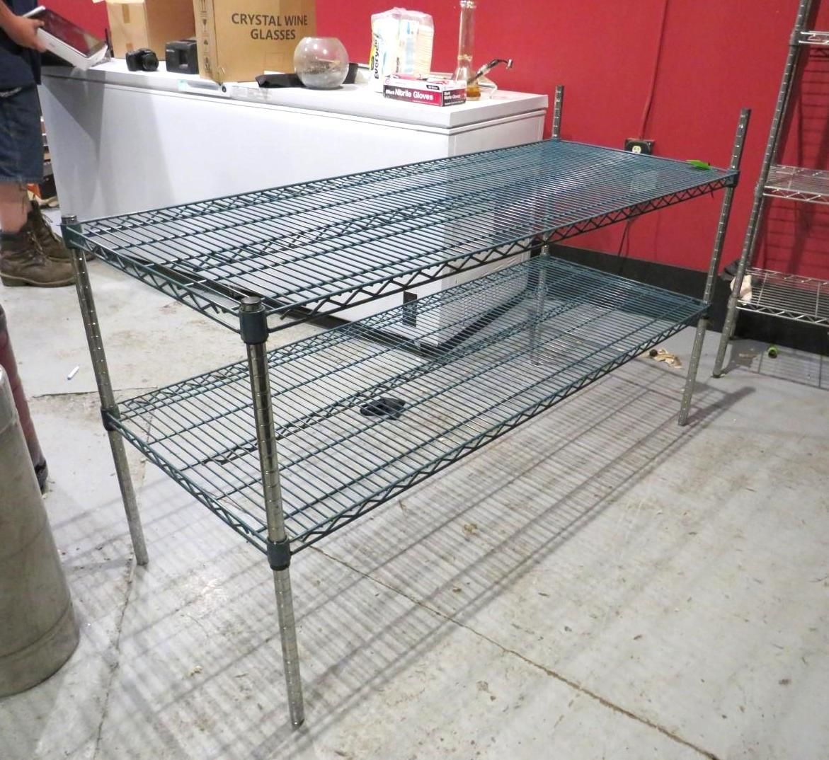 Metal wire shelving unit with two levels, in a room with a white table and red wall.