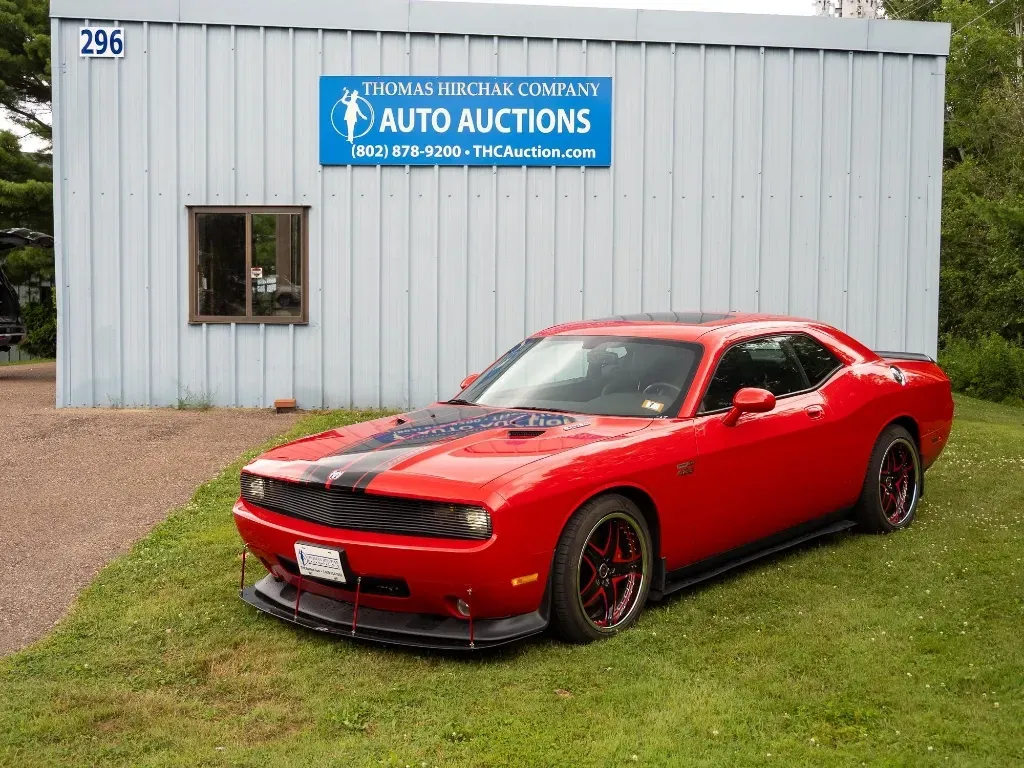 Red Dodge Challenger parked on grass in front of an auto auction building.