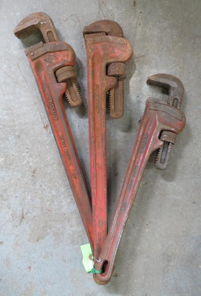Three red pipe wrenches on a concrete surface.