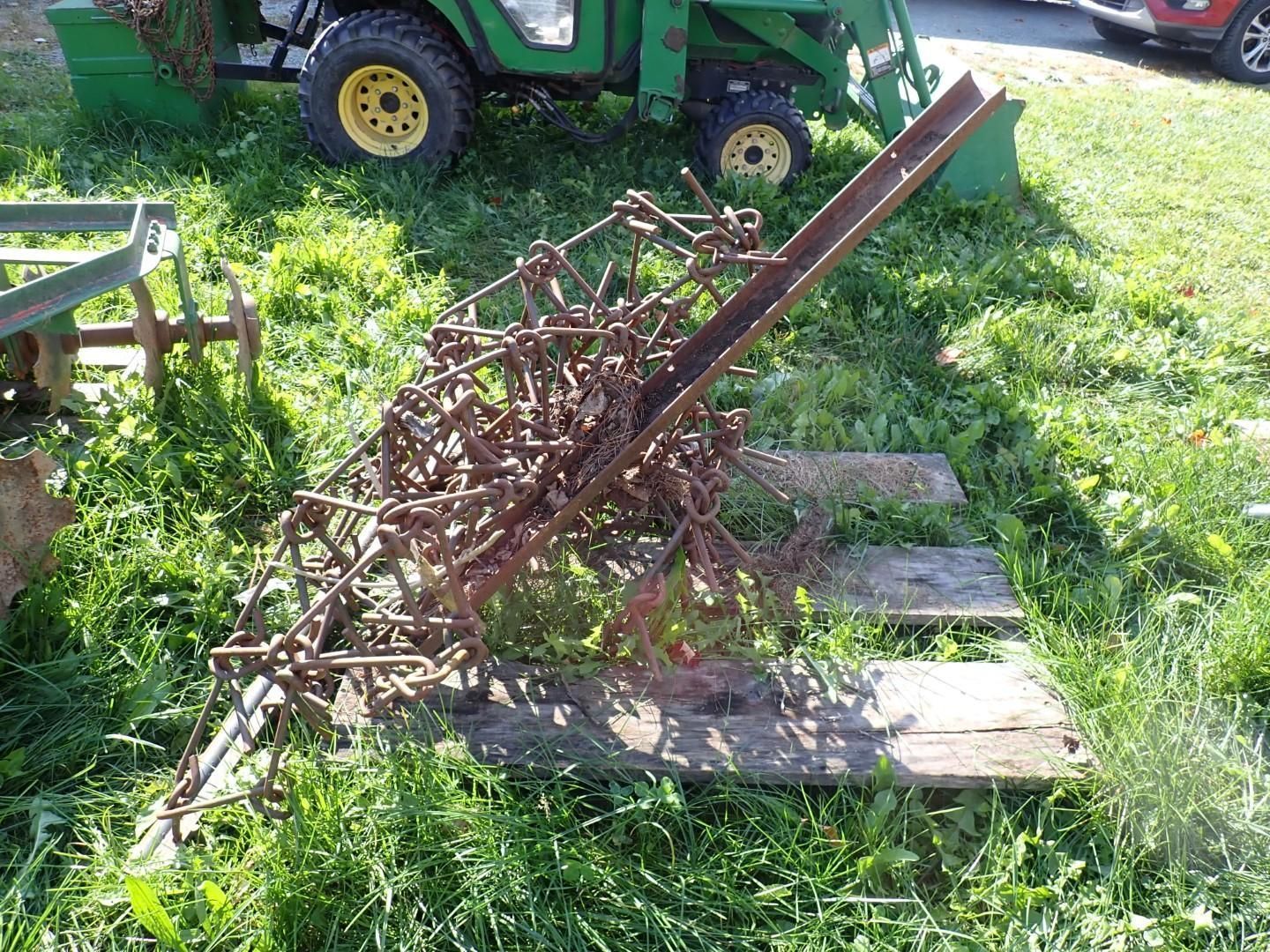 farm implement lying on grass beside stone pavers, with a green tractor in the background