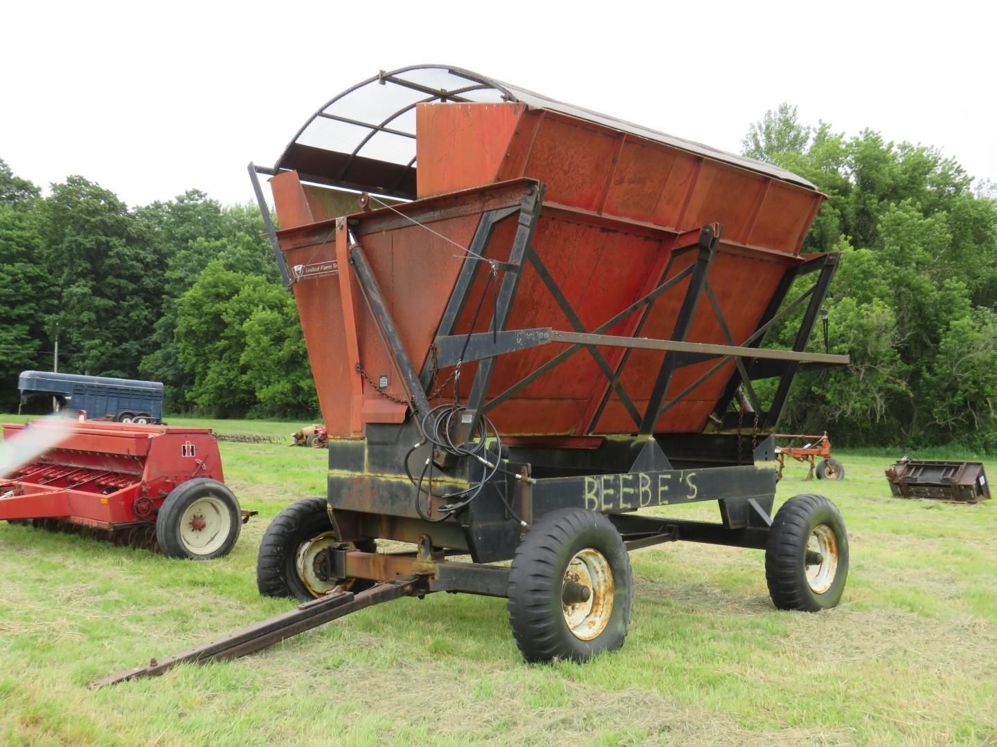 Red and black Reefer's hay wagon on a grassy field, next to other farm equipment.