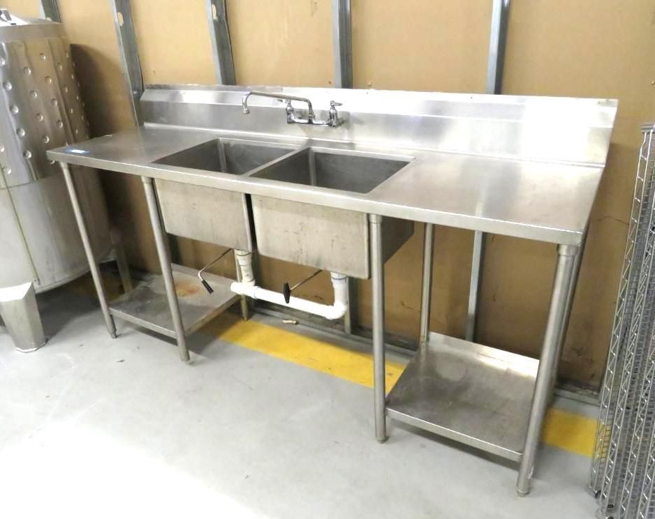 Stainless steel commercial two-basin sink with drain pipes and a backsplash, in a kitchen setting.