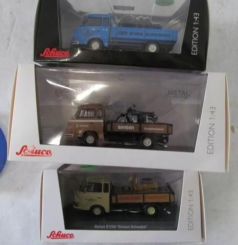 Three Schuco 1:43 scale model trucks in boxes: blue, brown, and tan.