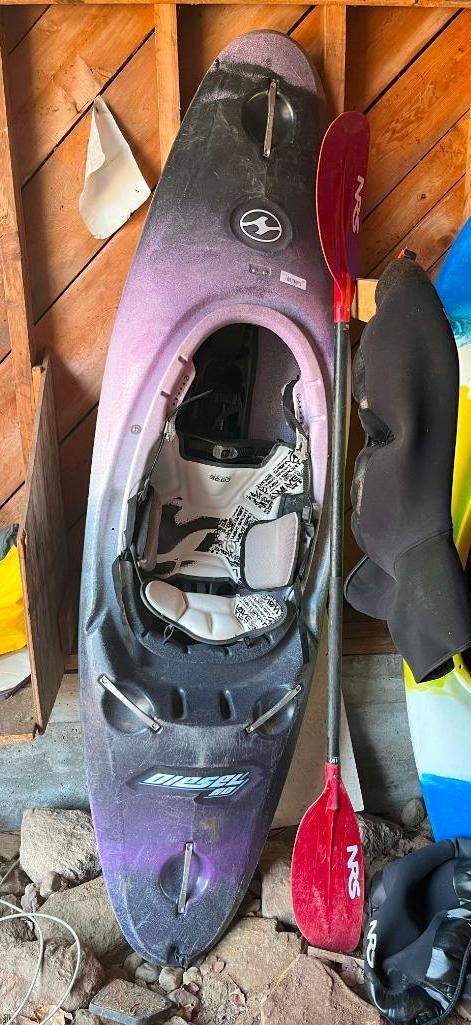 A purple and black kayak with a red paddle against a wooden wall.
