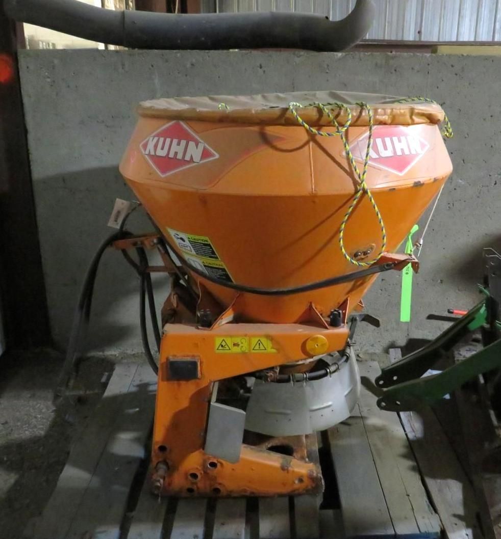 Orange Kuhn fertilizer spreader on a wooden pallet; orange cover held down by rope.