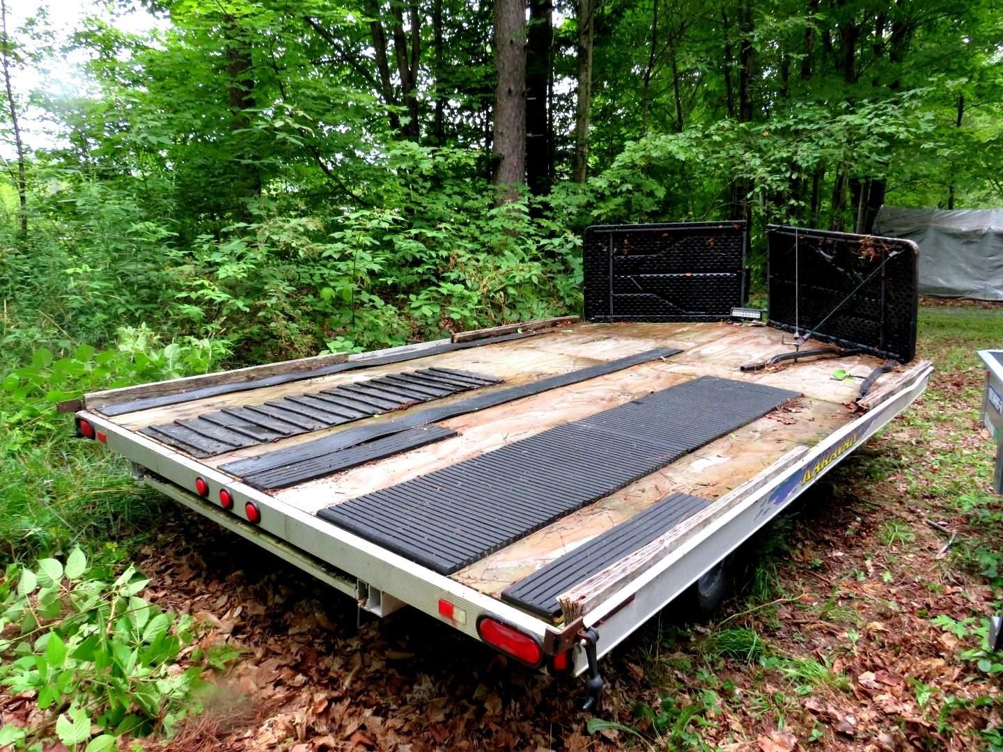 Flatbed trailer with black rubber mats, set in a wooded area.