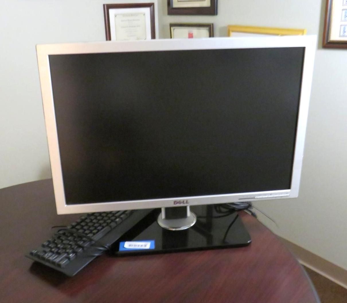 Dell computer monitor and keyboard on a dark wooden desk.