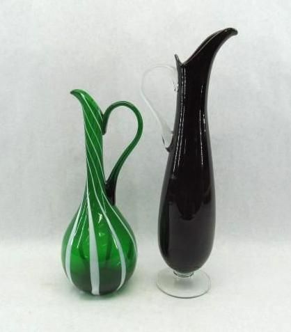 Two tall glass pitchers: green striped and dark red, on a white surface.