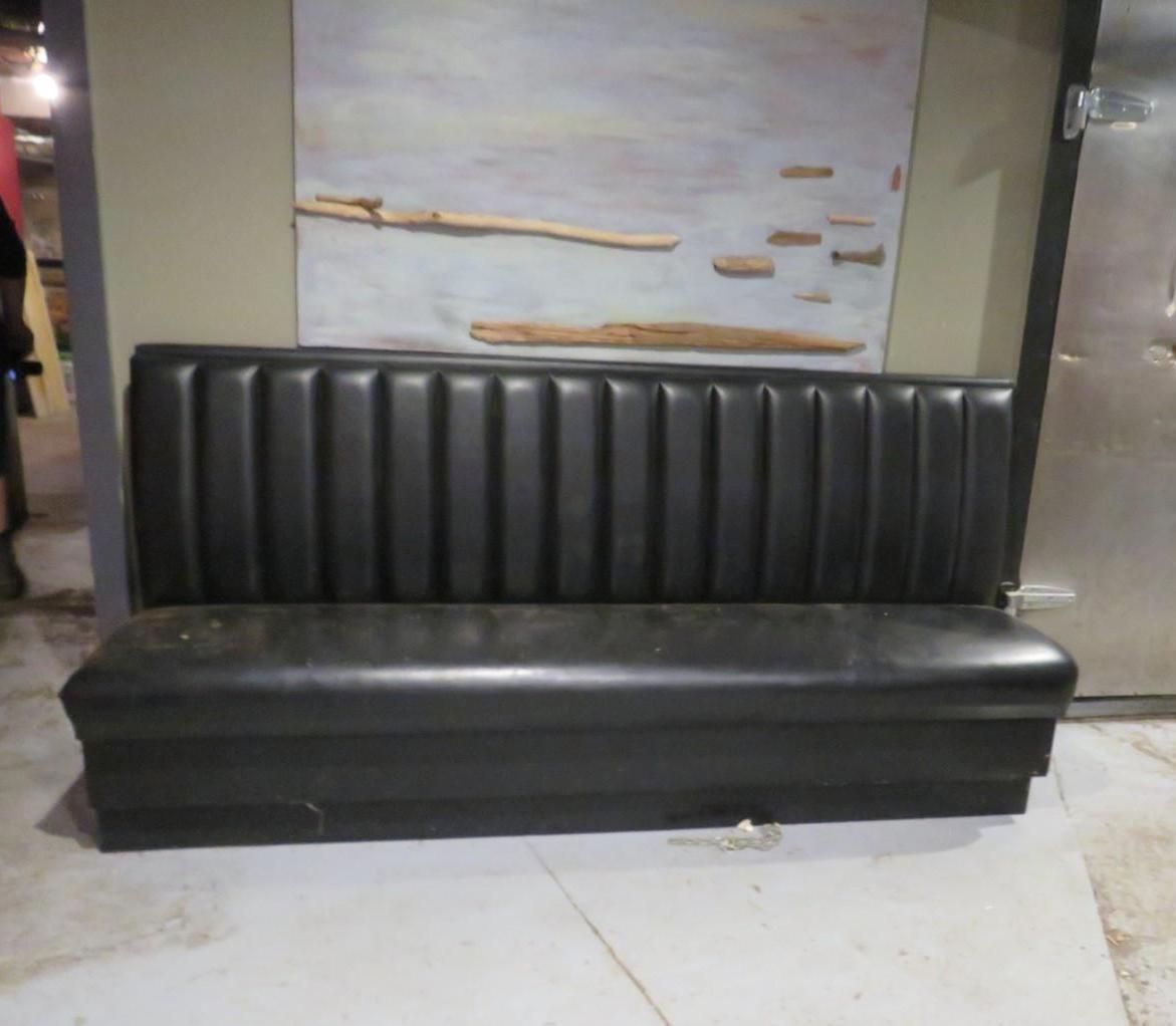 Black booth seating against a wall with a mural and a metal door.