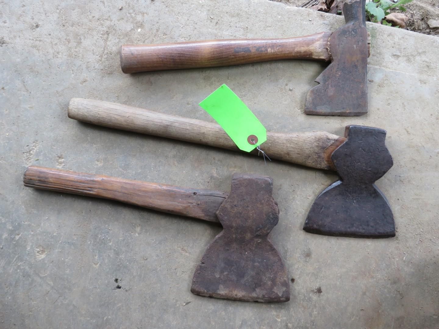 Three axes with wooden handles on a concrete surface.
