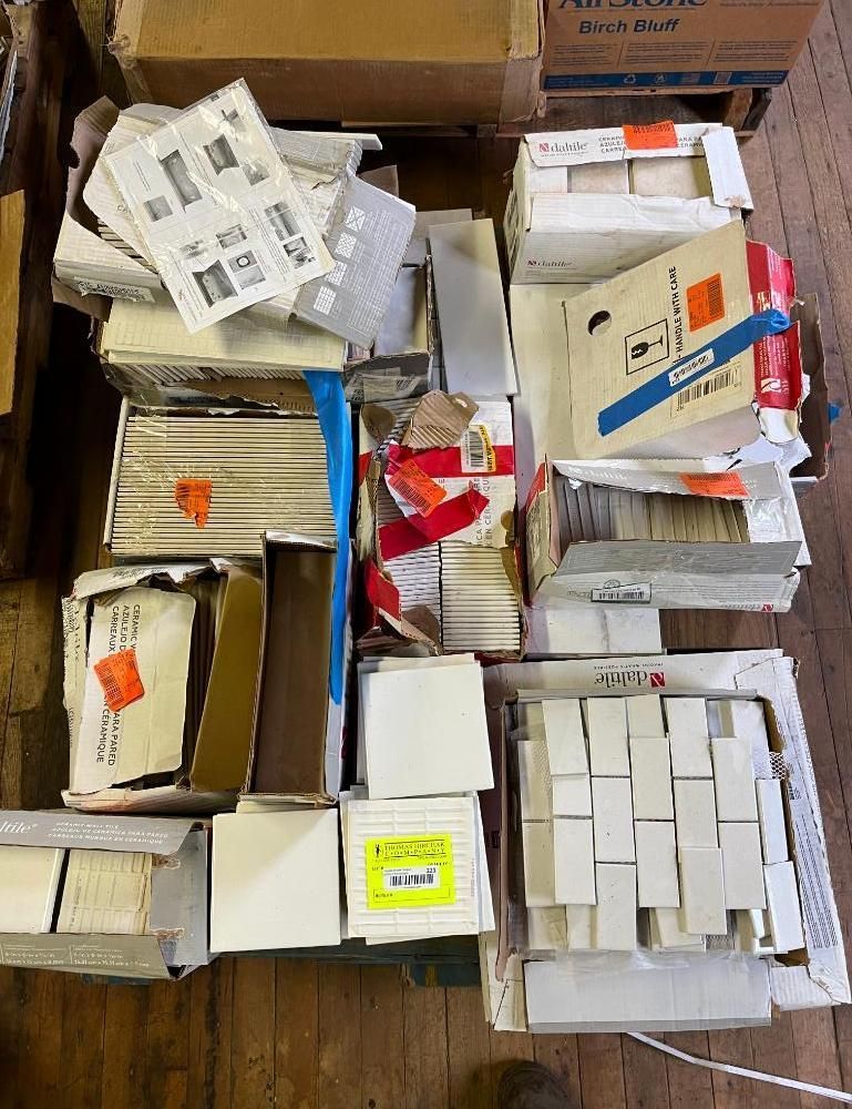 Boxes of white and neutral-toned tiles, papers, and packaging are stacked on a wooden pallet.