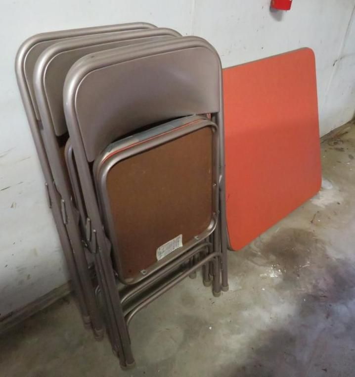 Stack of tan metal folding chairs and a red square table against a gray wall.