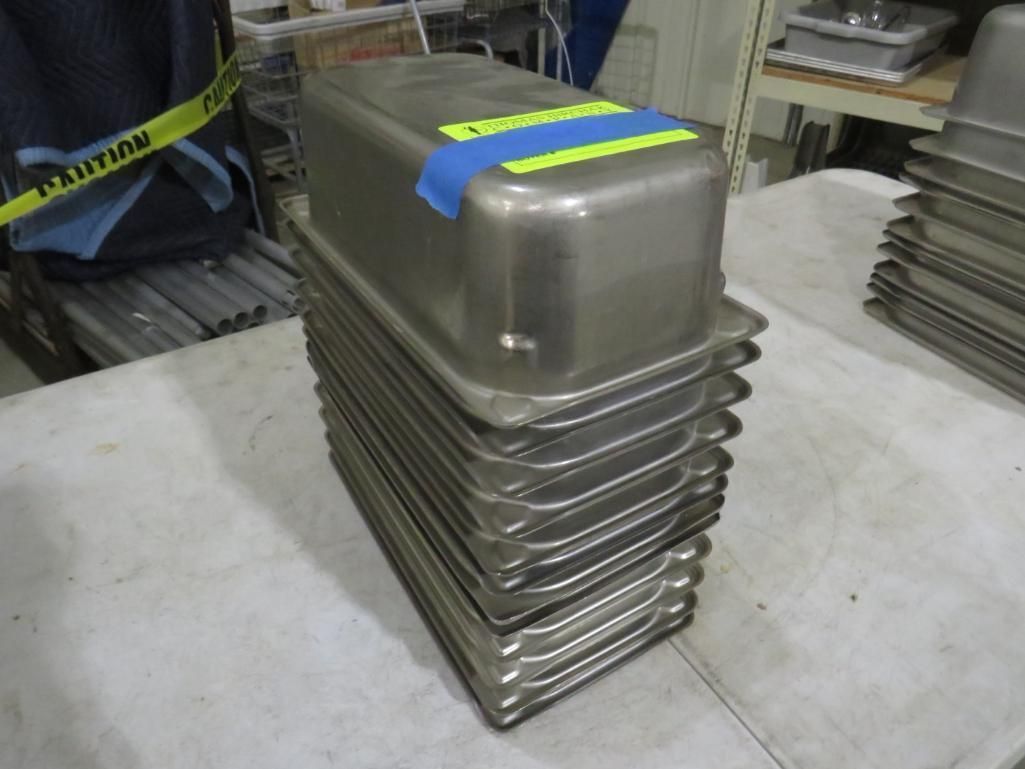 Stack of stainless steel food pans on a white surface, with a yellow and blue tape.