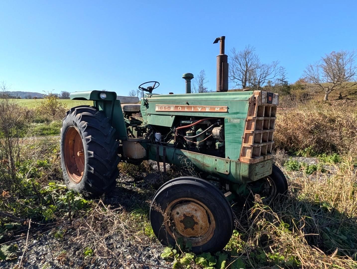 green tractor in a field on a sunny day, with bare trees and distant hills in the background