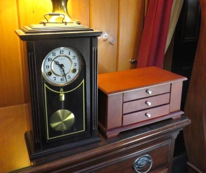 A dark wooden clock with a gold pendulum and a jewelry box on a dresser.