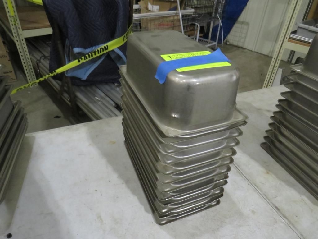 Stack of stainless steel rectangular pans on a white surface, with caution tape in the background.
