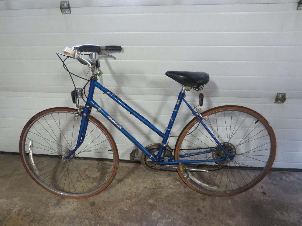 Blue vintage bicycle with brown tires in front of a white garage door.