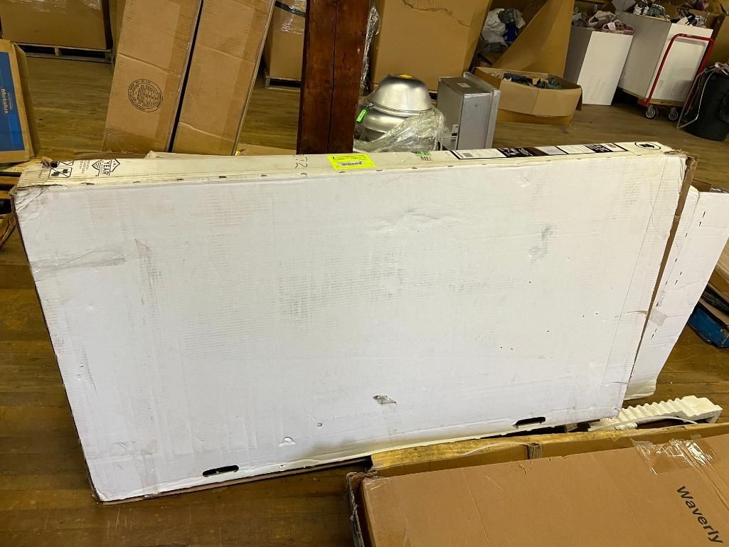 Large white appliance panel on a wooden floor, with boxes and other items in the background.