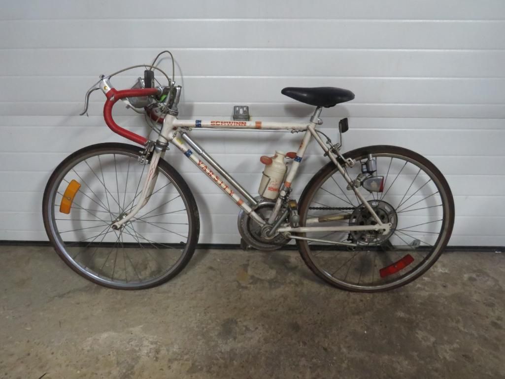 White and red road bike with water bottle cage, against a white panel wall.