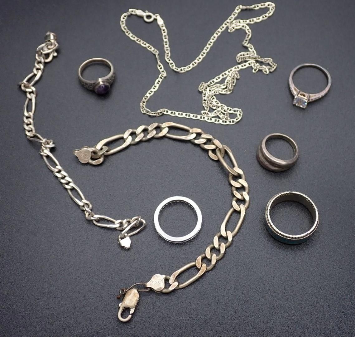 Jewelry: silver necklace, bracelet, and rings with gemstones, arranged on a dark surface.