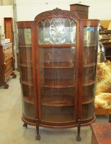 Curved wooden display cabinet with glass doors and shelves; stained glass top panel, carved details, claw feet.