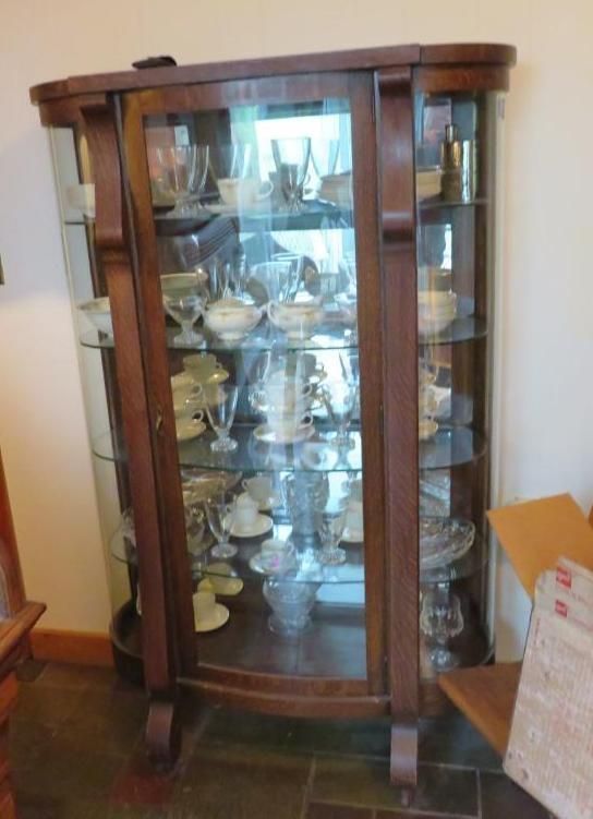 Wooden curio cabinet with glass shelves displaying dishware in a room.