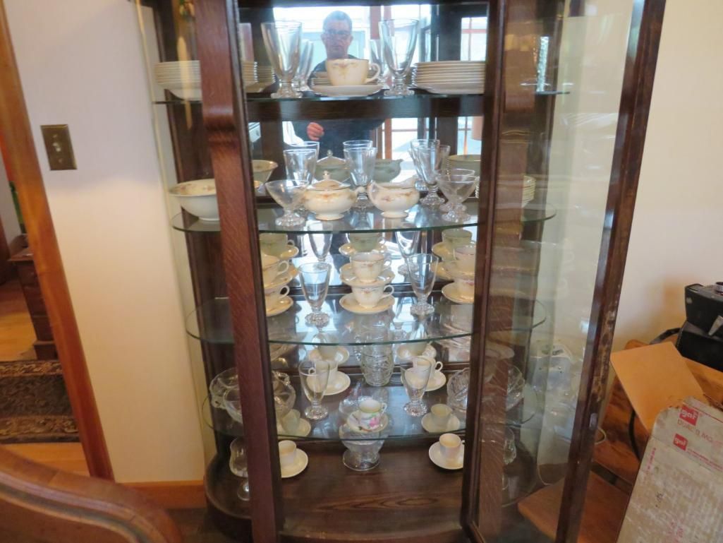 Wooden china cabinet with glass shelves displaying dishes and glassware.
