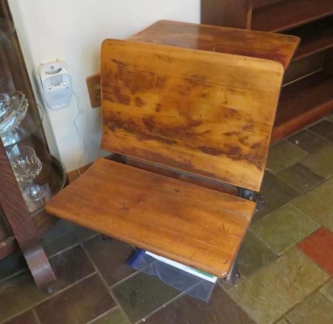 Wooden antique school desk with hinged tabletop and seat, next to a white wall.
