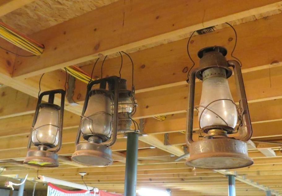 Four antique oil lanterns hanging from a wooden ceiling.