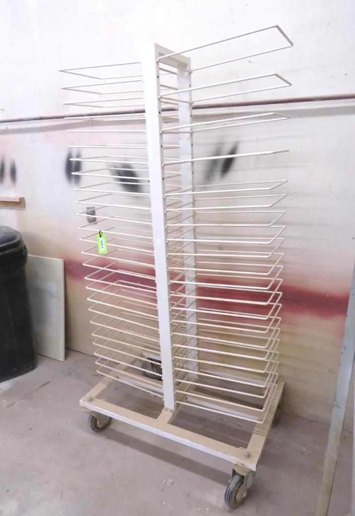 White drying rack on wheels in a workshop, multiple shelves for holding items.