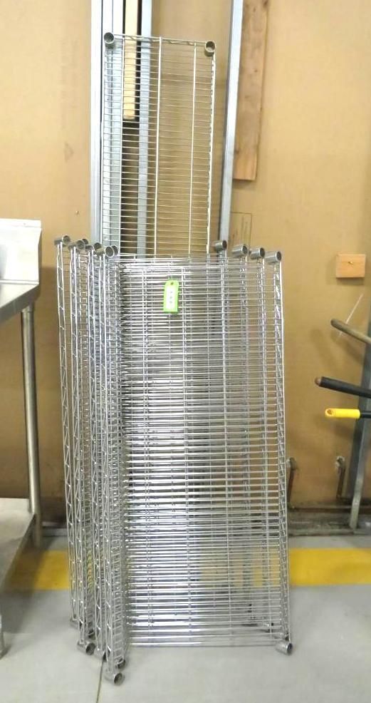Stack of chrome wire shelving units with wheels, against a wall.