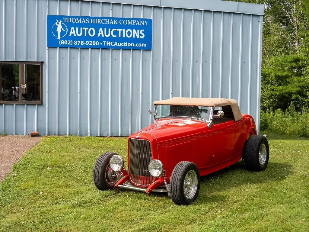 Red hot rod convertible parked in front of an auto auction building.