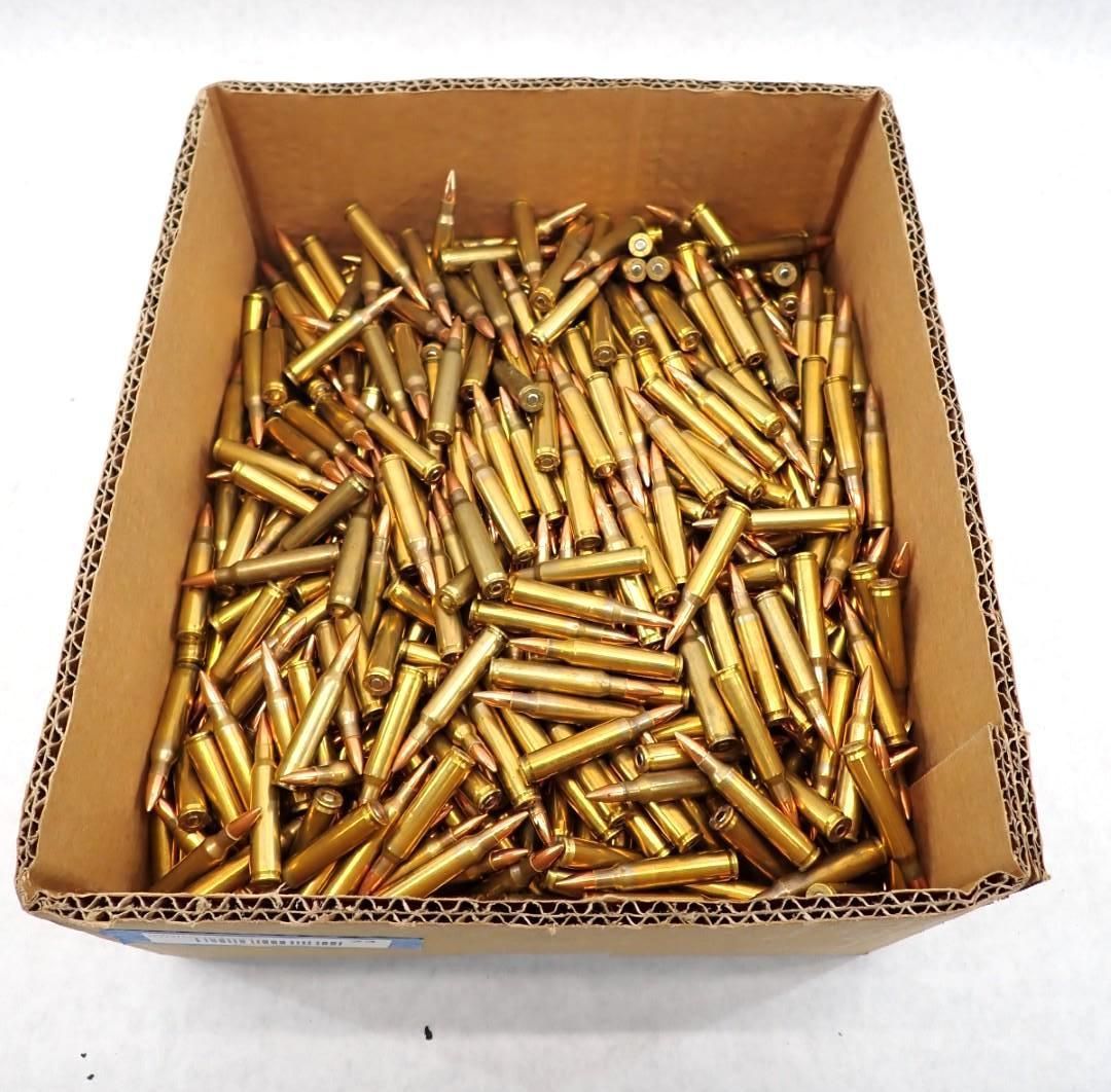 Box filled with brass-colored rifle cartridges. Brown cardboard box, white background.