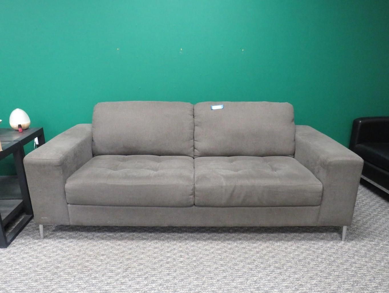 Gray two-seater sofa with tufted back and silver legs in front of a green wall and patterned carpet.