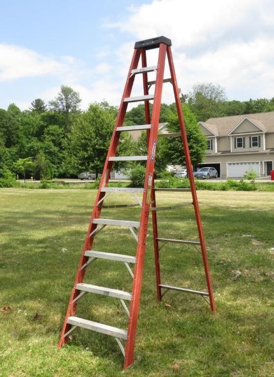 Red A-frame ladder on a grassy lawn.