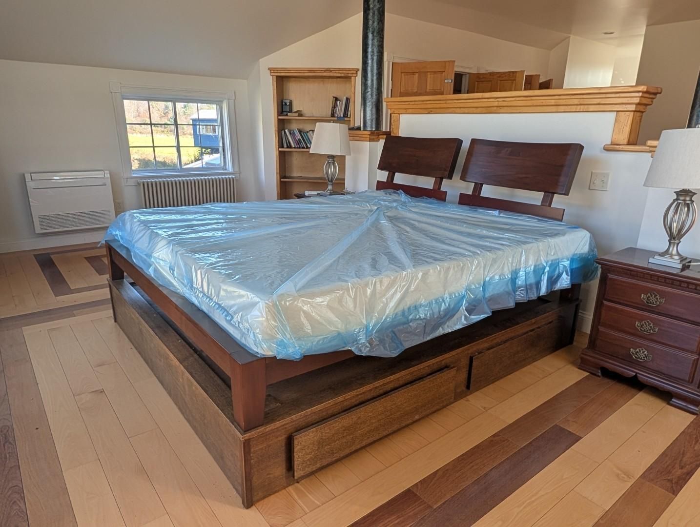 Wooden bed with blue plastic-covered mattress in a sunlit attic bedroom