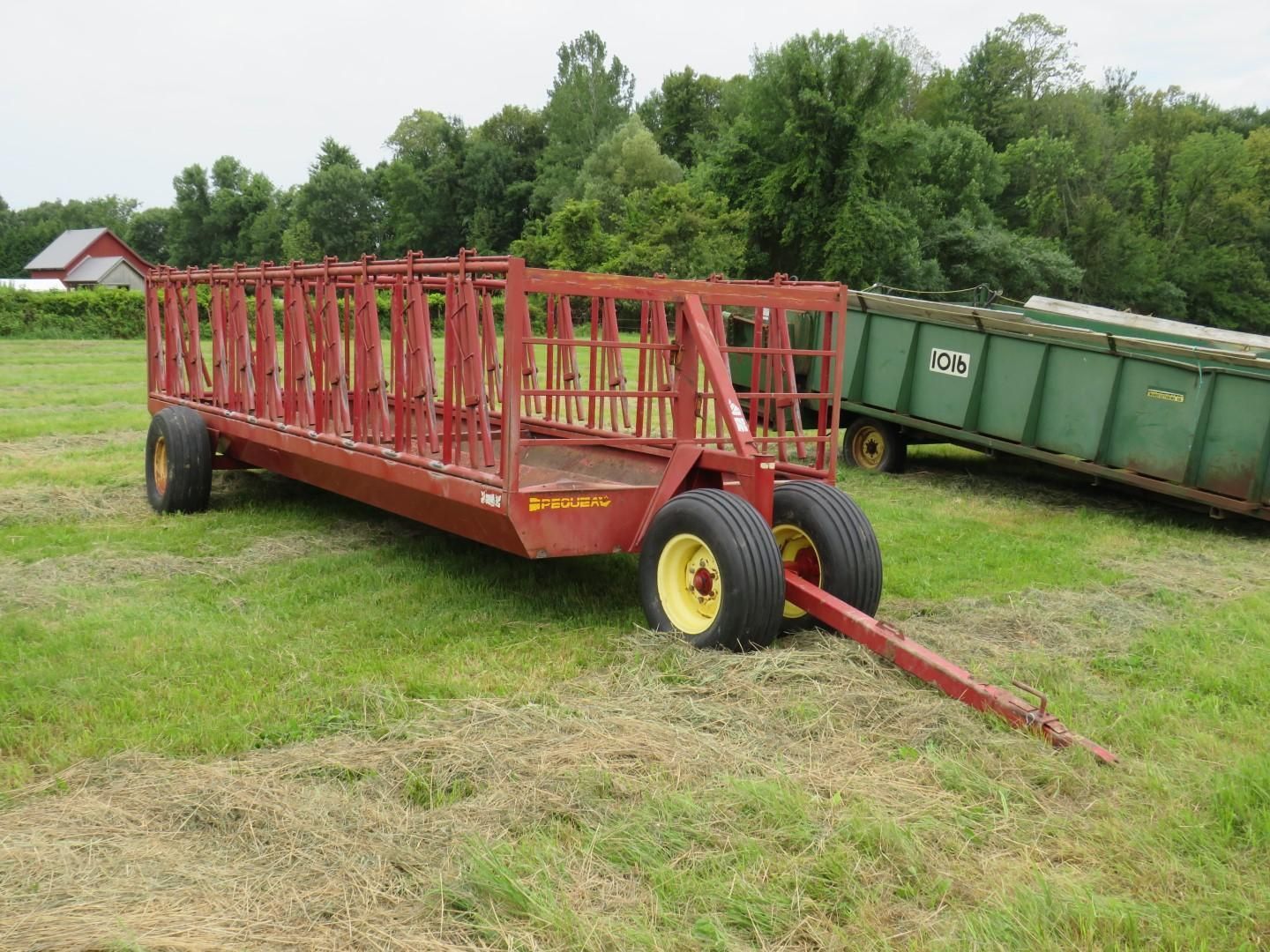 Red hay wagon with yellow wheels parked in a grassy field.