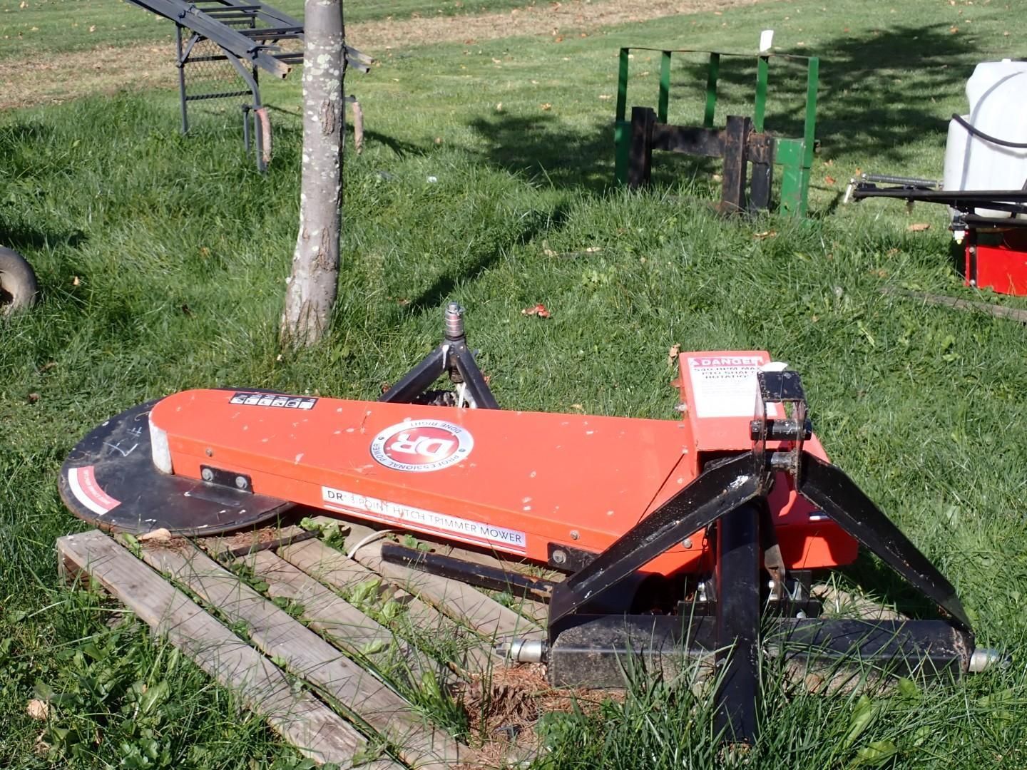 Orange farm mower attachment resting on wooden pallets in a grassy yard