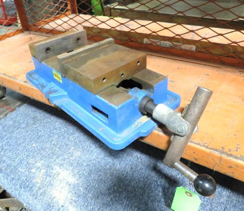 Blue metal vise on an orange cart with a gray surface. It has a handle and is in a workshop setting.