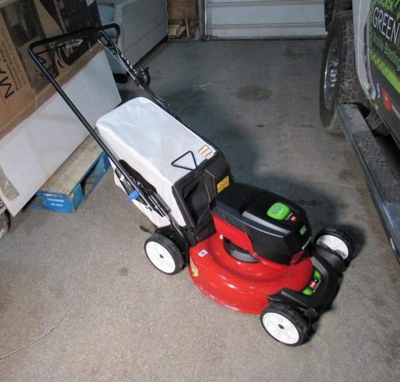 Red and black Toro lawnmower with a white grass bag, on a concrete surface.