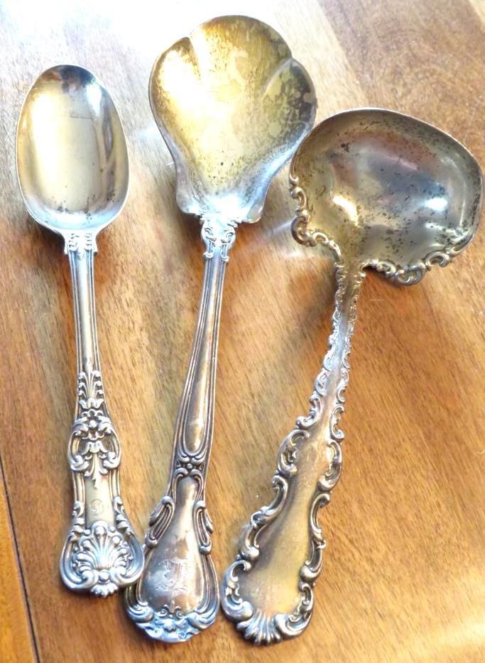 Three ornate silver spoons on a wooden surface.