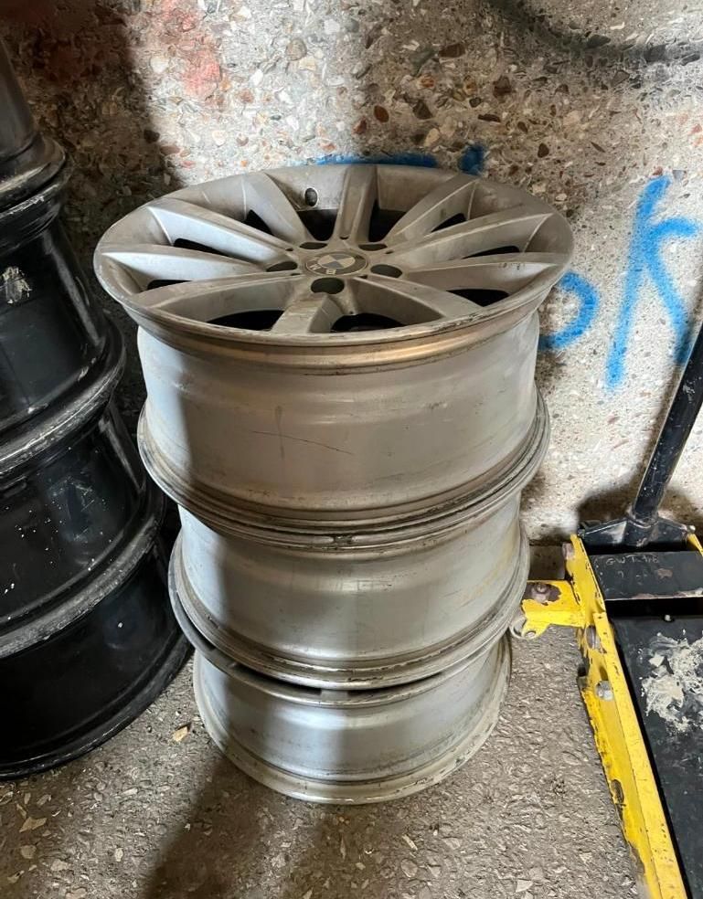 Three silver car rims stacked on top of each other. A black rim stack is to the left.